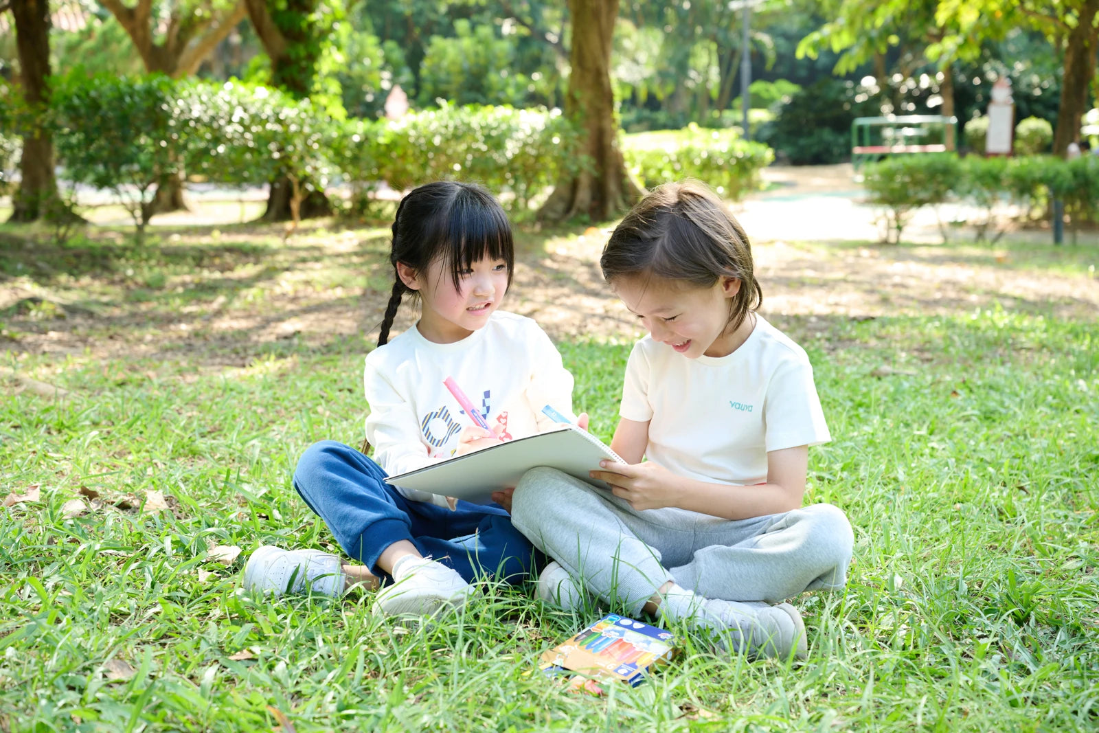 Two children sharing a book outdoors in Vauva FW26 clothing