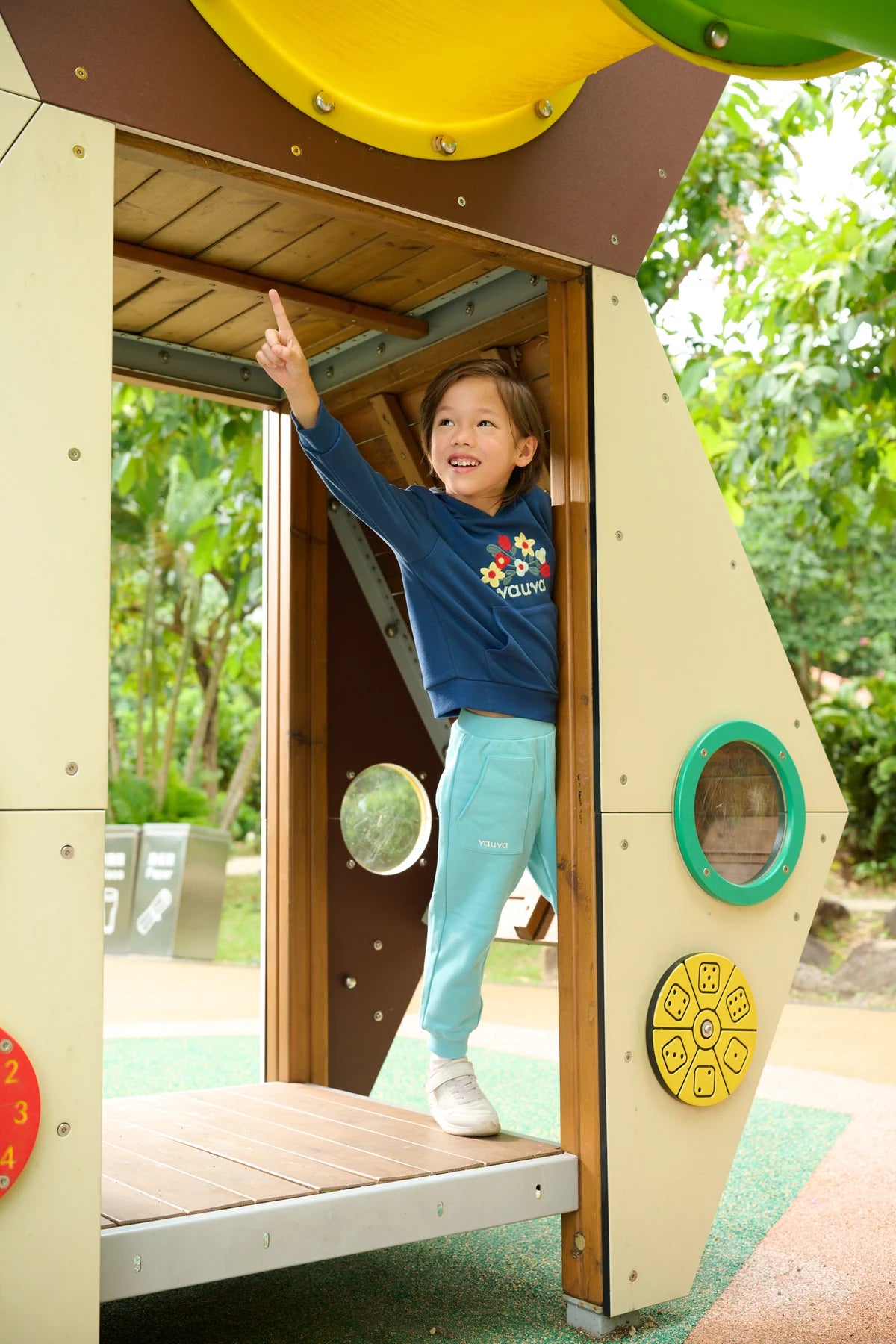 A child in teal joggers and a navy hoodie, exploring a playground.