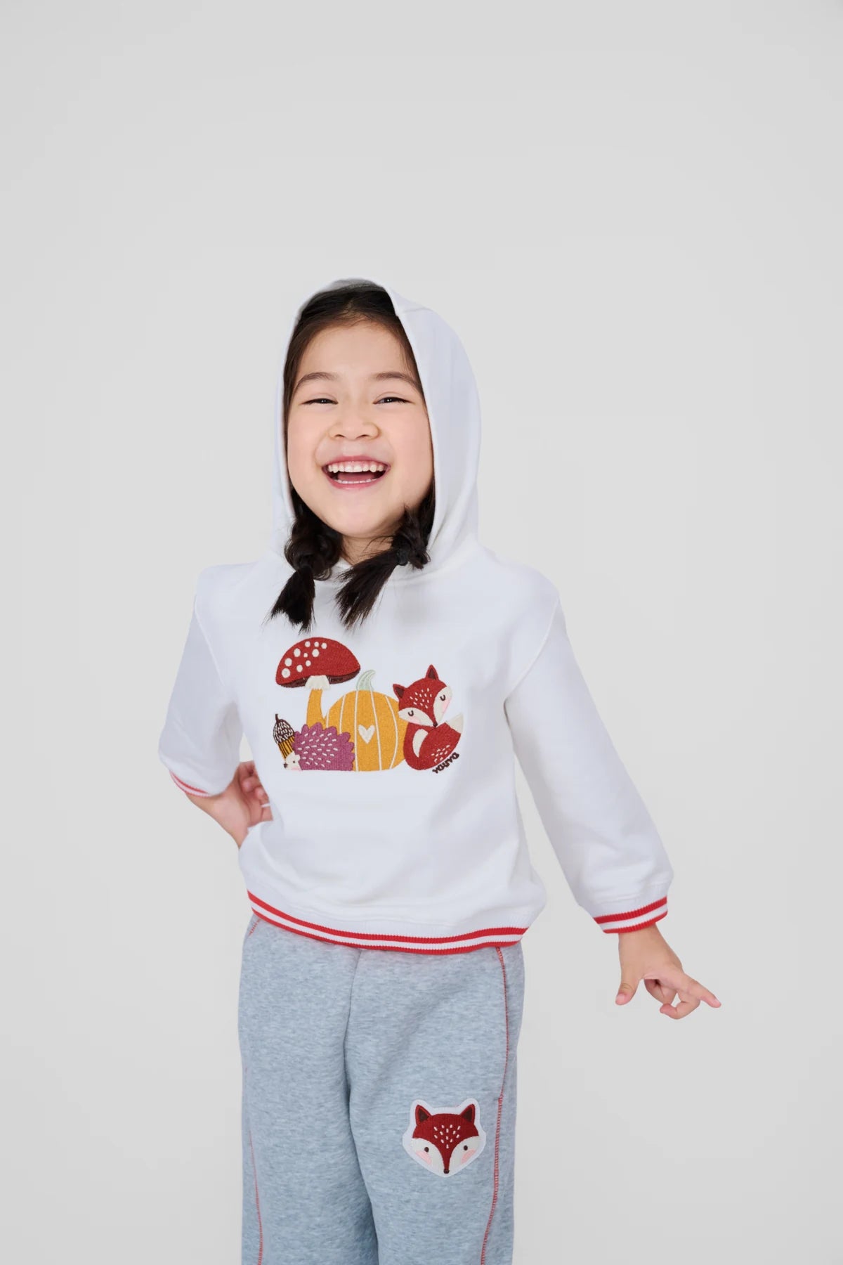Girl laughing in a white woodland embroidered hoodie from Vauva FW26.