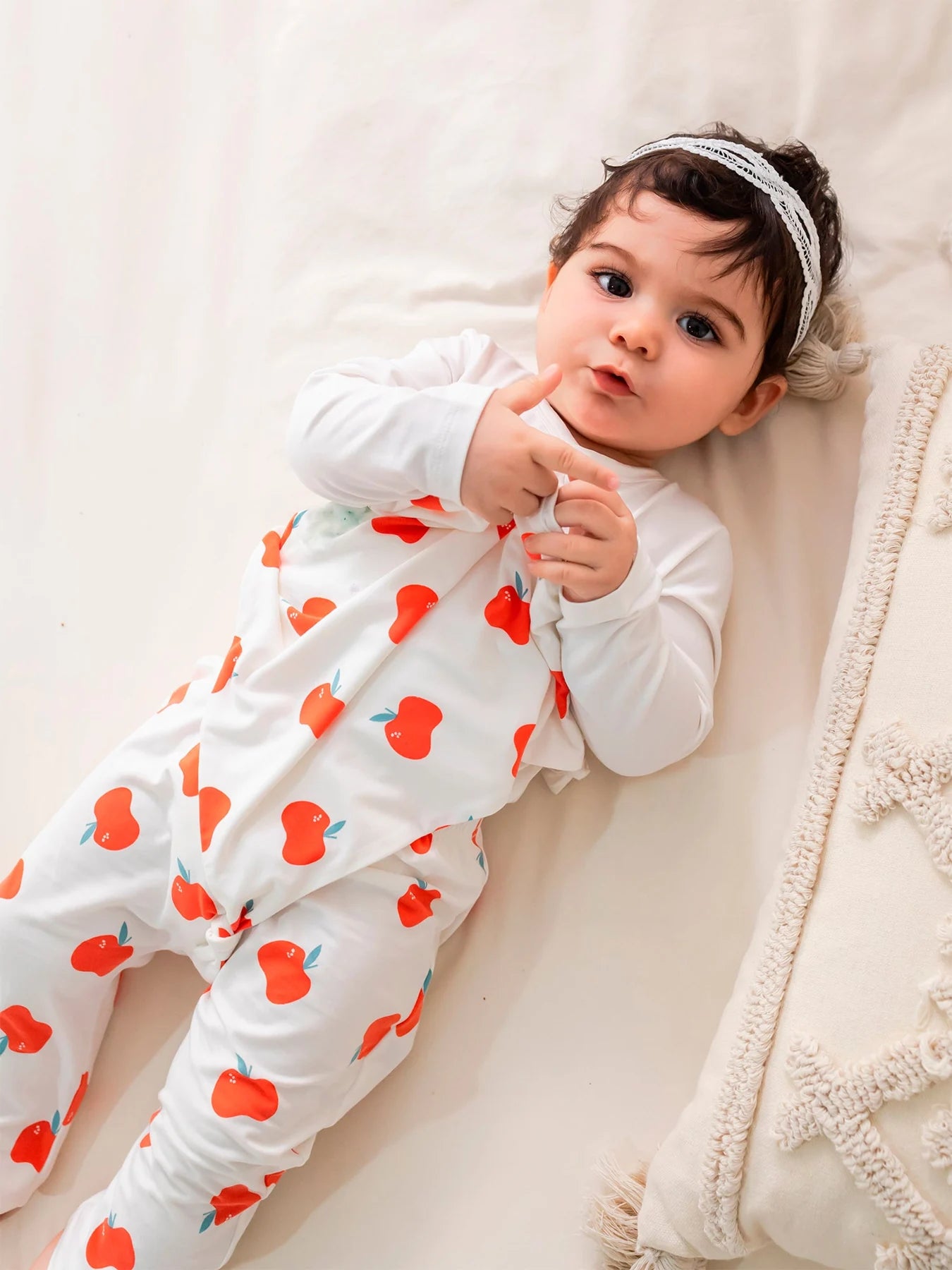 Baby in an apple-print BBNS outfit resting on cream bedding.