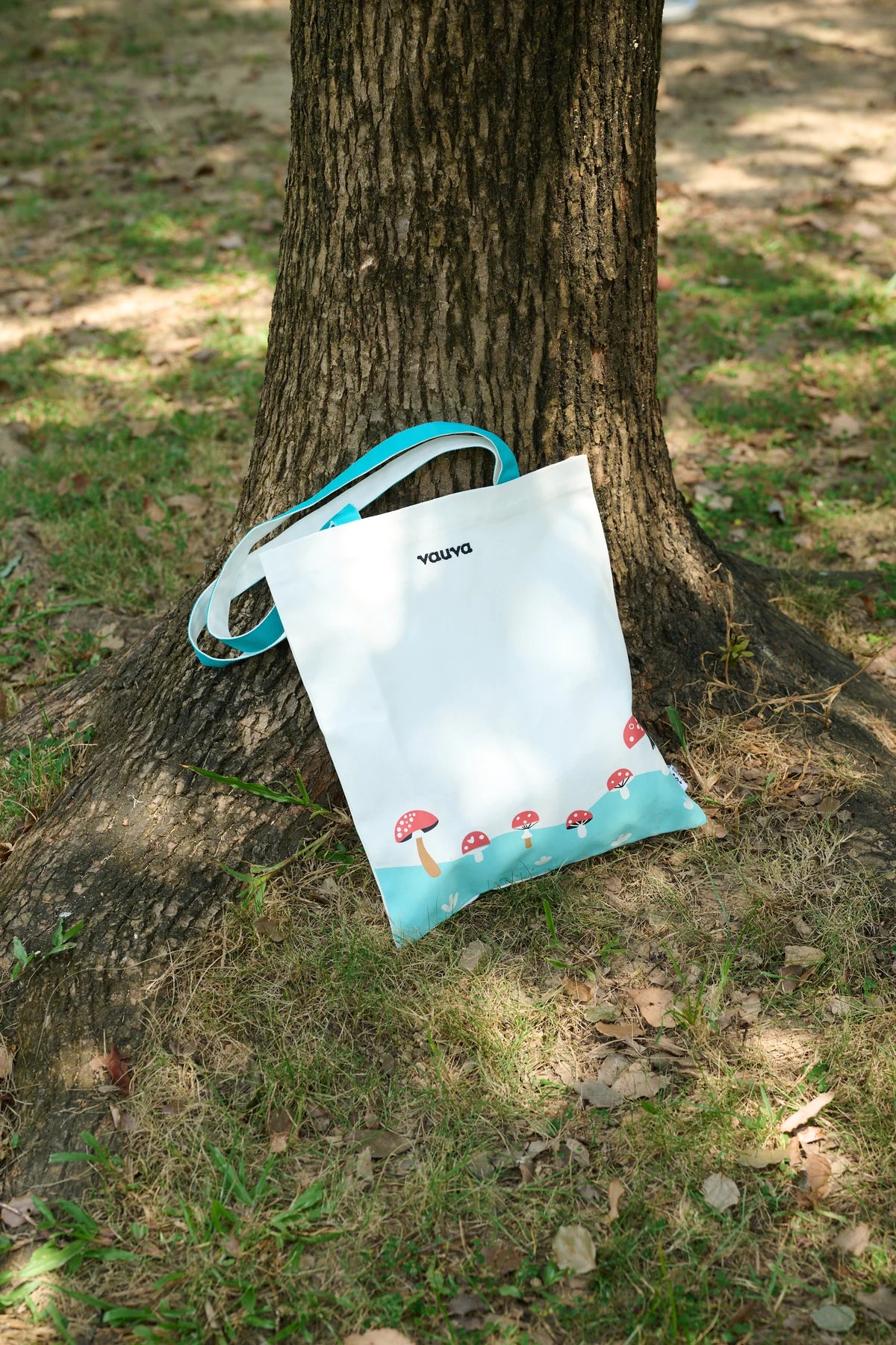 A white and teal mushroom-print canvas bag hanging against a tree.