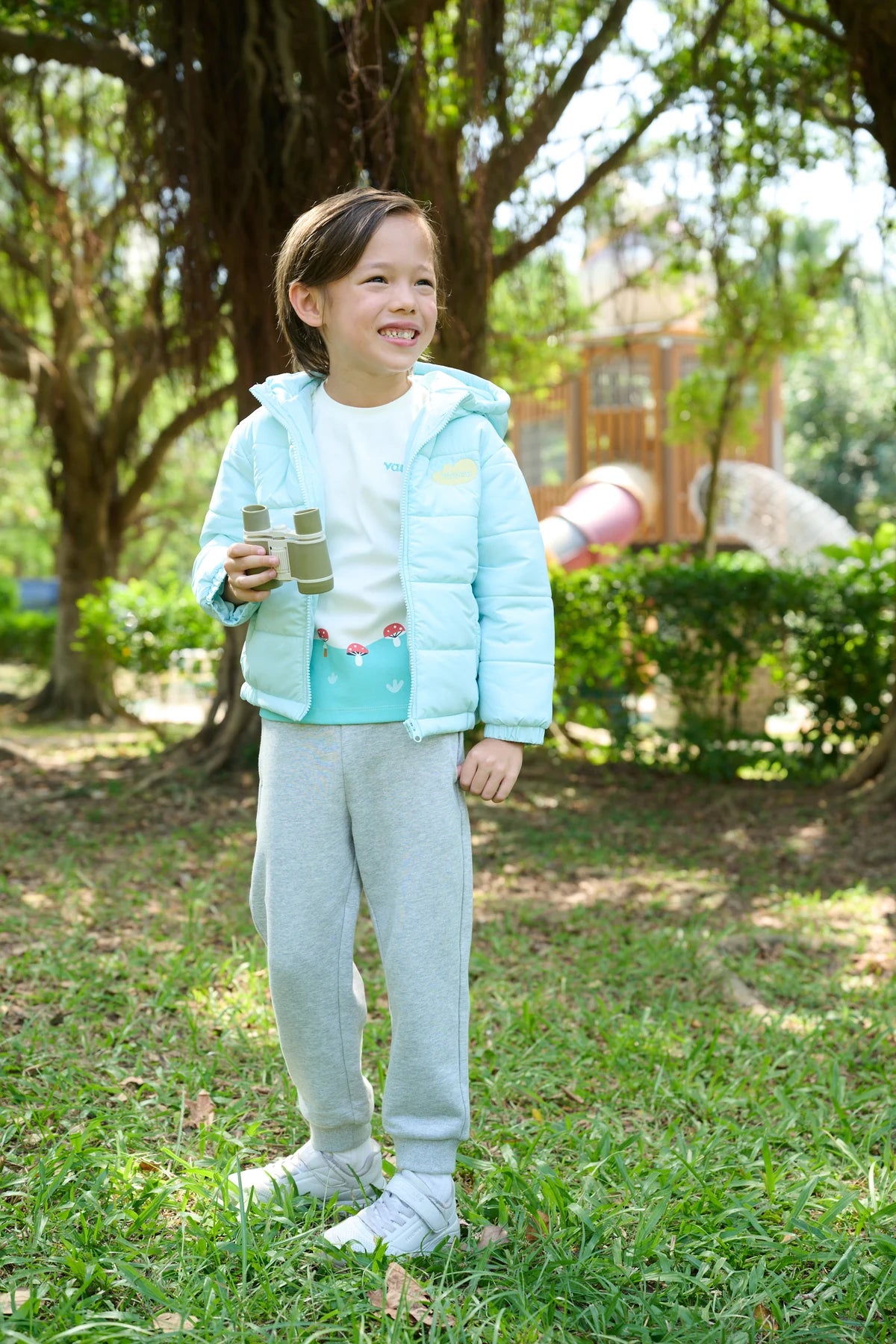 A child in a pale teal puffer jacket with a woodland-print canvas bag.