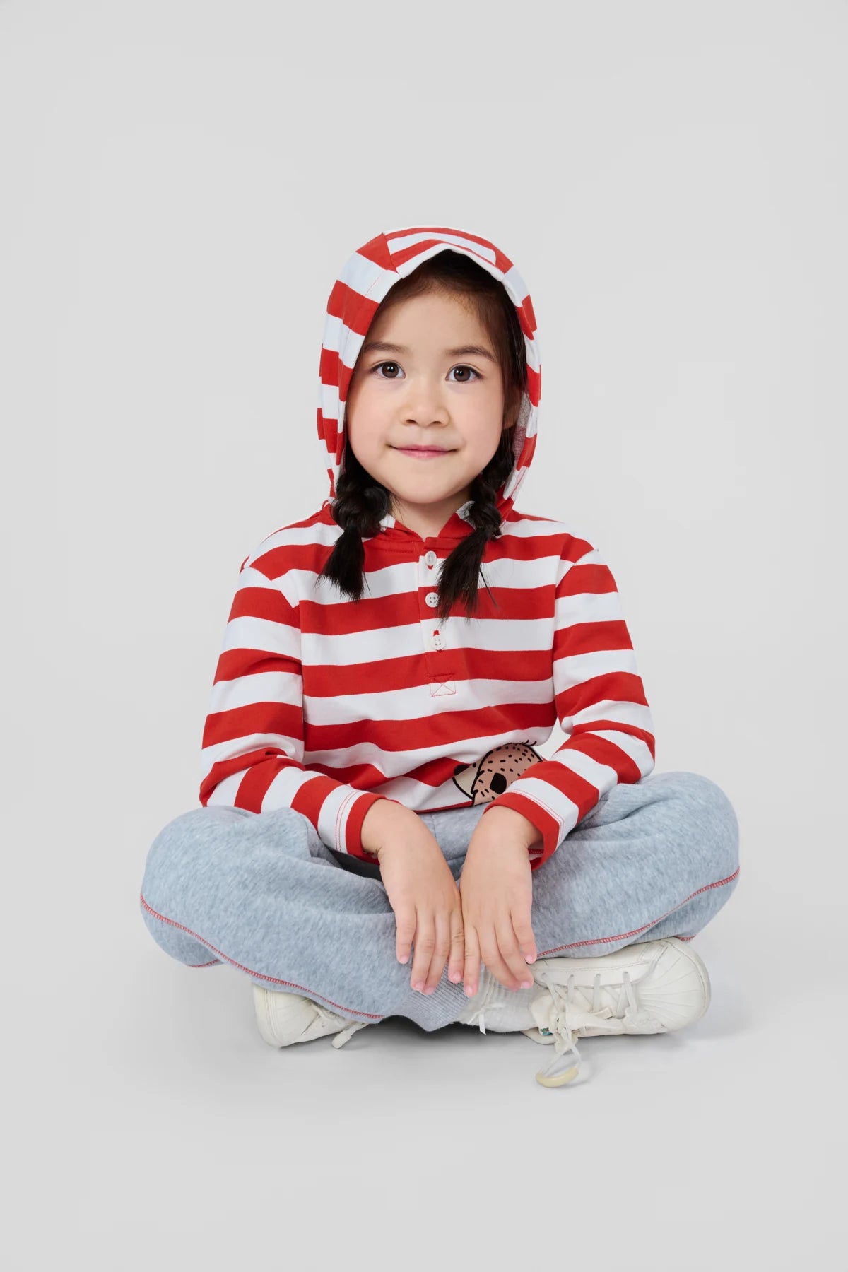 Girl seated in a red striped hedgehog tee and grey joggers.