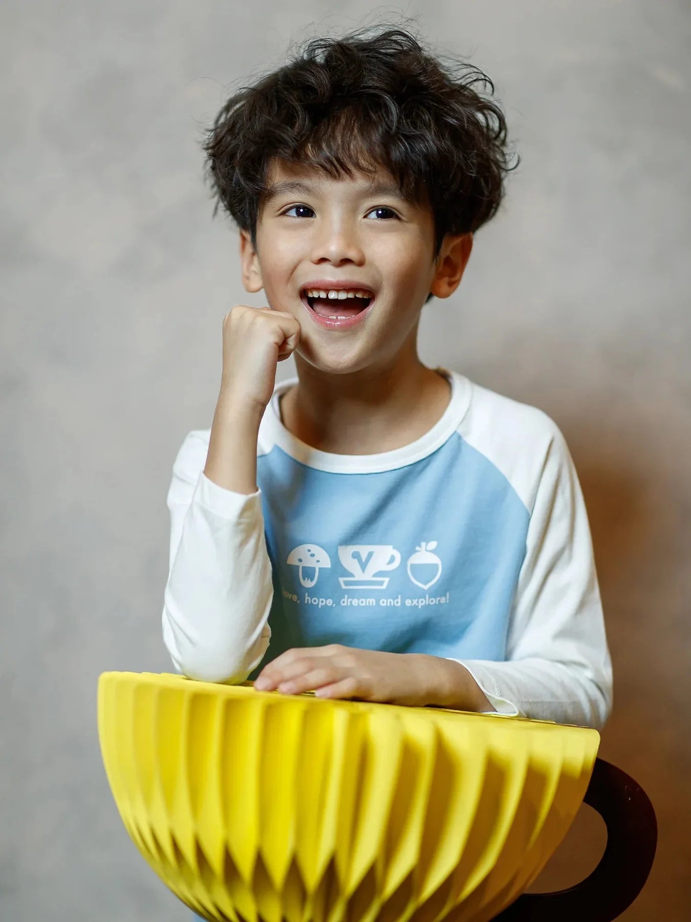 A child in the blue-and-white icon raglan top beside a yellow cup prop.