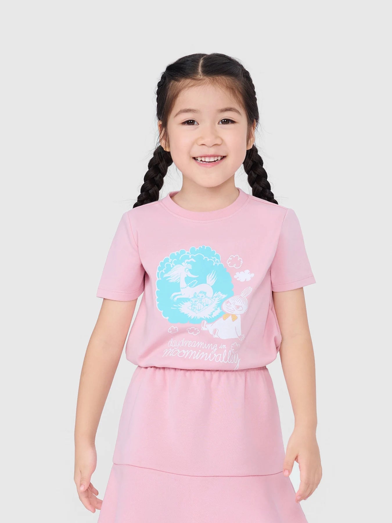 Girl smiling in the pink Little My graphic T-shirt, styled with a pink skirt.
