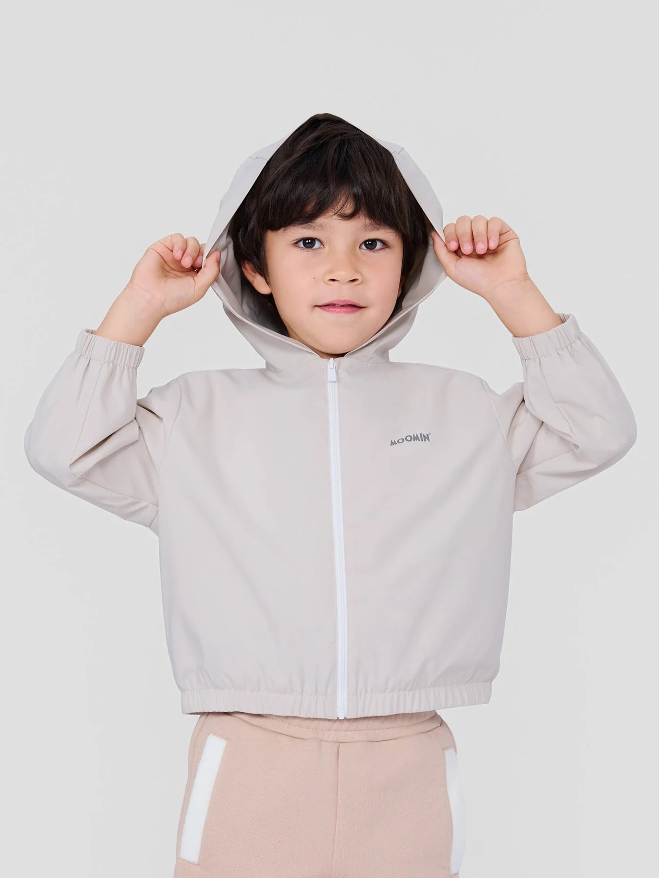 Boy wearing the ivory Stinky lightweight jacket with its hood up.