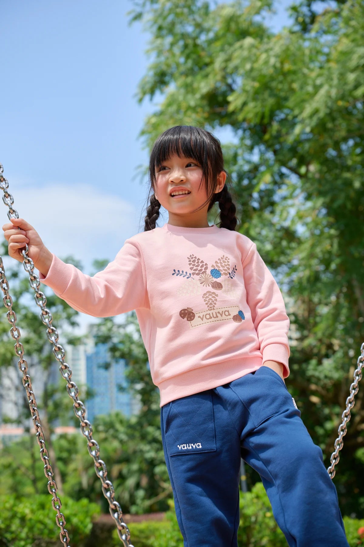 A smiling child in a pink Vauva FW26 sweatshirt outdoors
