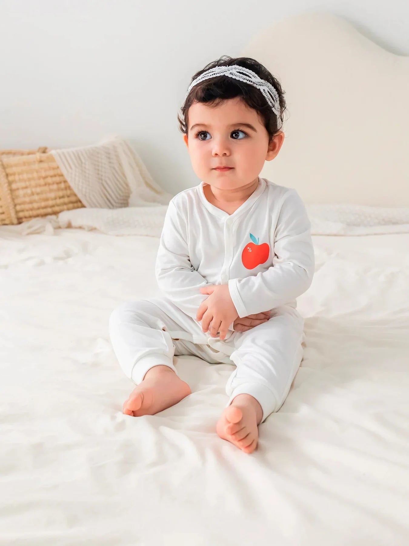 A baby in the white apple-motif long-sleeved romper.
