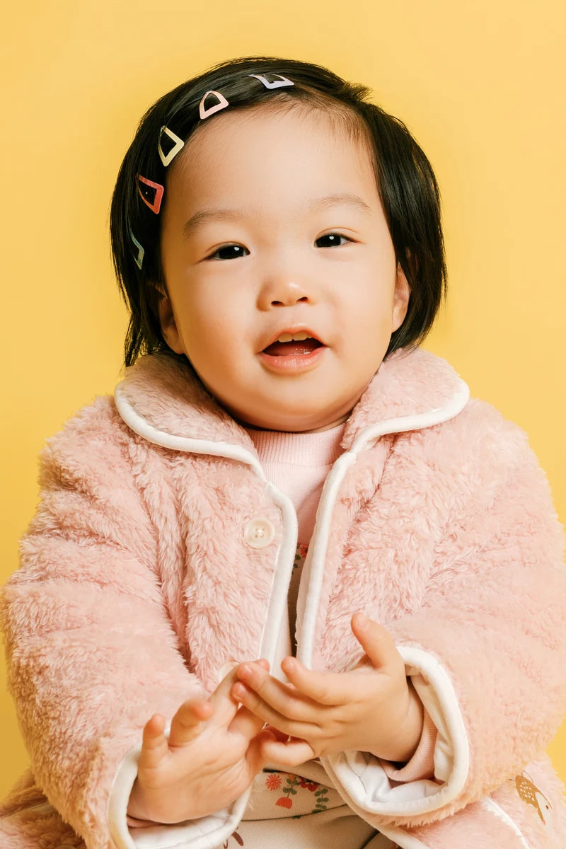 A smiling baby wearing a soft pink jacket. Face of Vauva 2025.