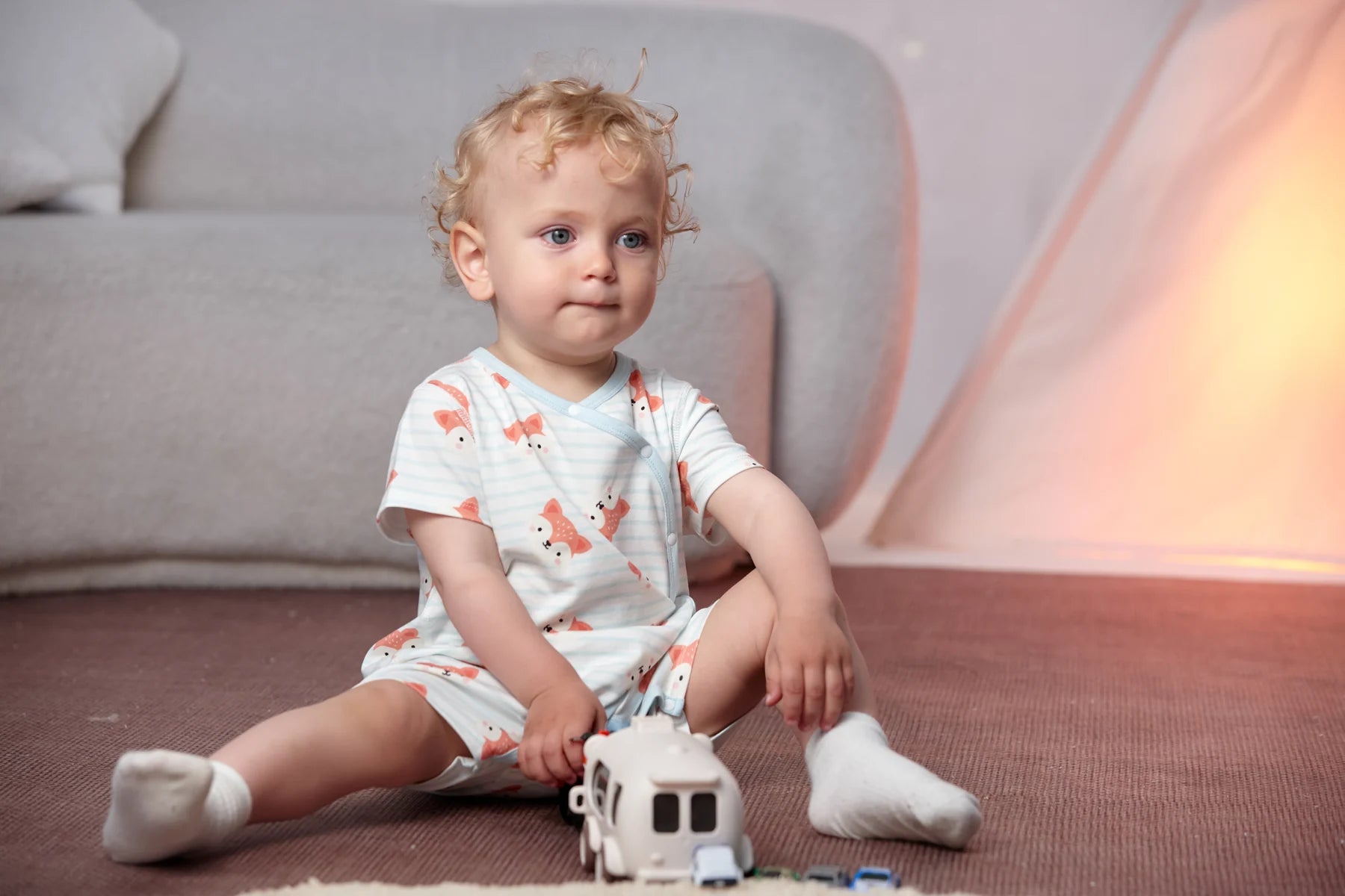 A toddler plays with a toy vehicle in the fox all-over-print romper and pale blue fox bib from the four-piece set.
