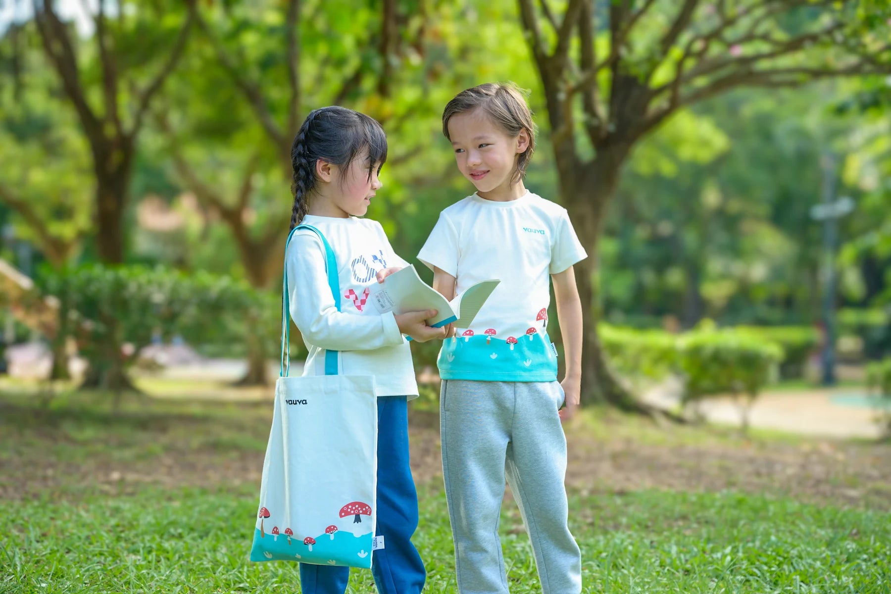 Two children sharing a book beneath the trees in Vauva FW26 woodland styles.