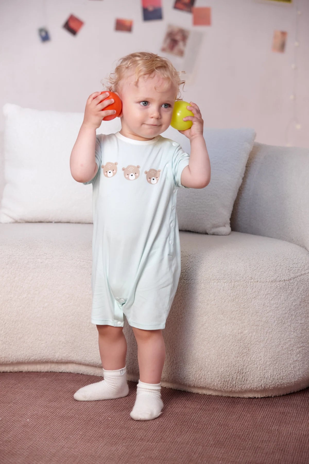A toddler holds colourful toys in the mint bear graphic romper from the four-piece gift set.