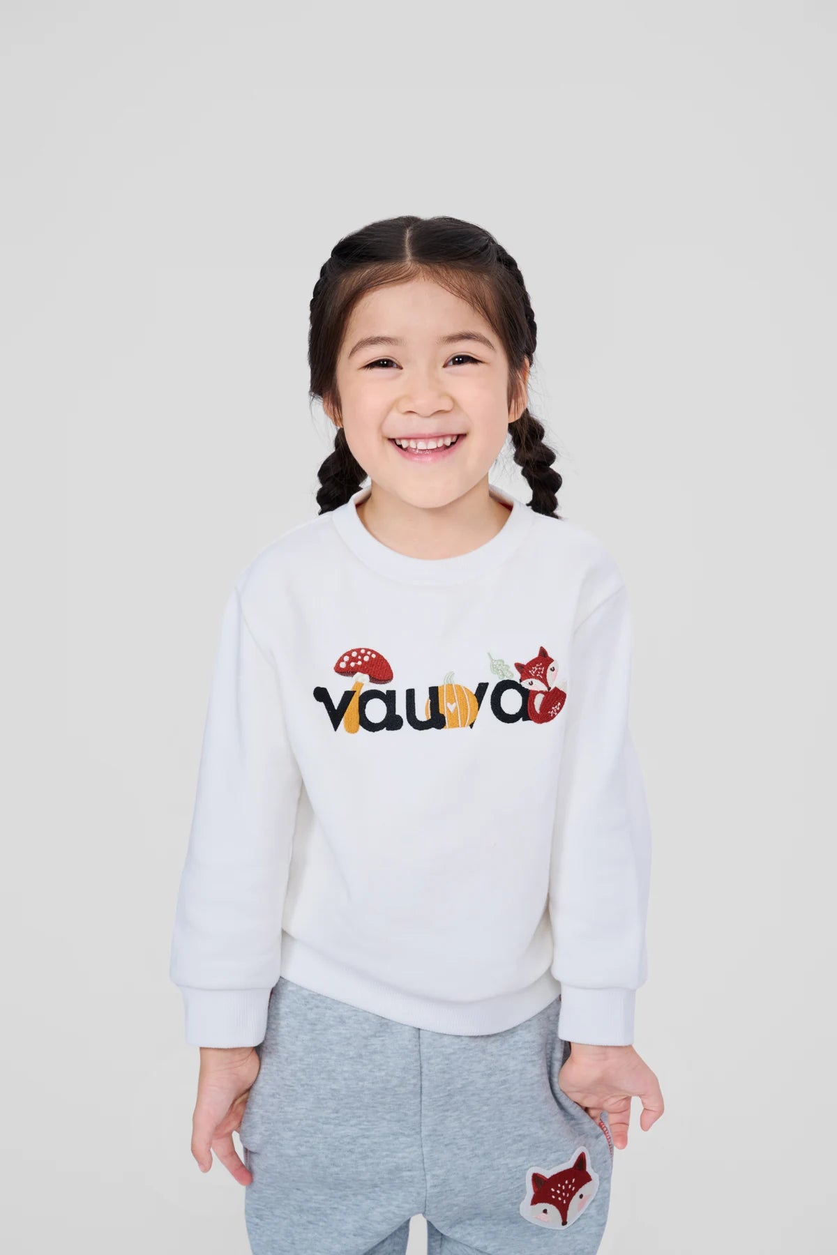 Smiling girl in the woodland logo sweatshirt and grey fox patch joggers.