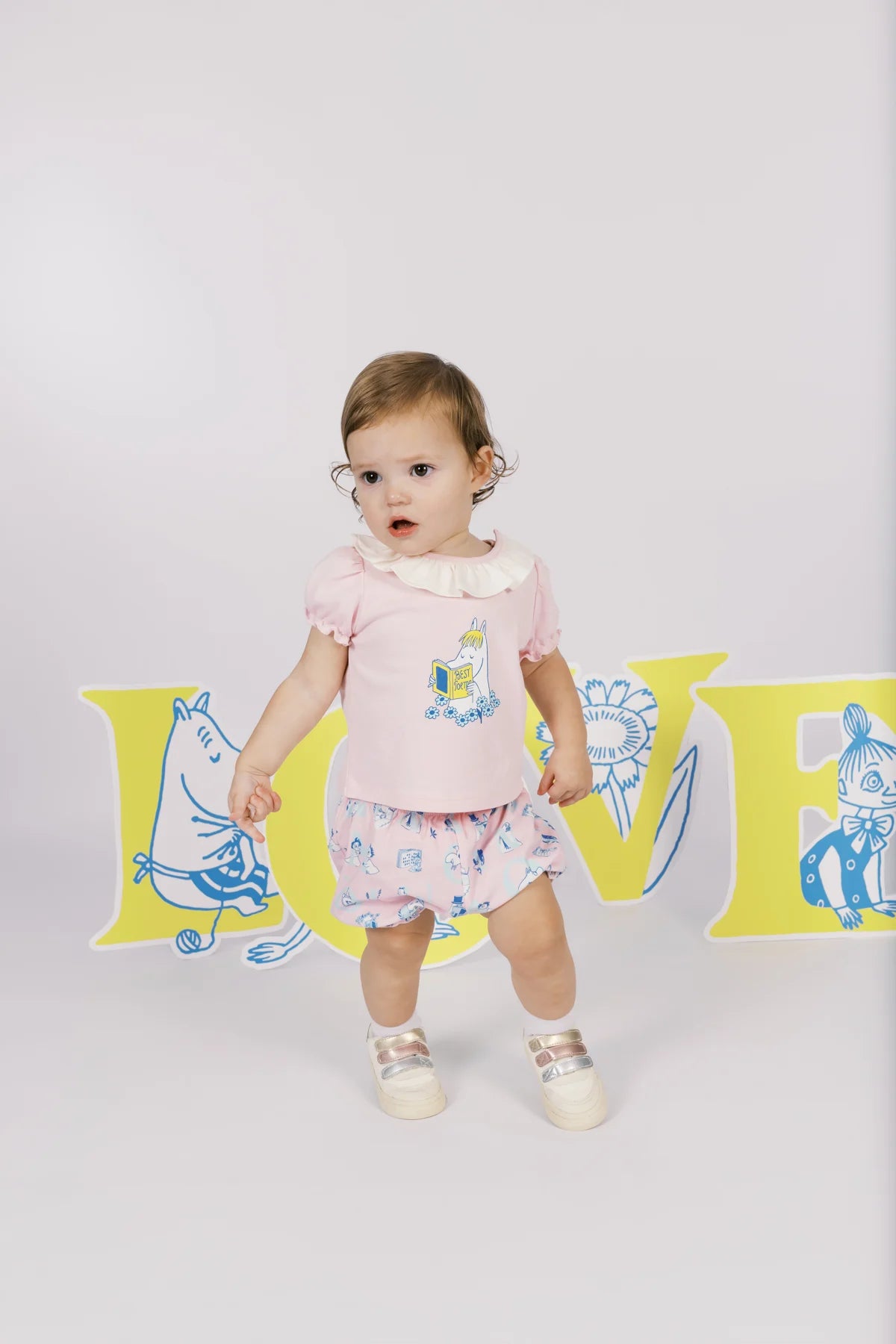 Baby wearing a pink Moomin graphic T-shirt and coordinating pink printed shorts.