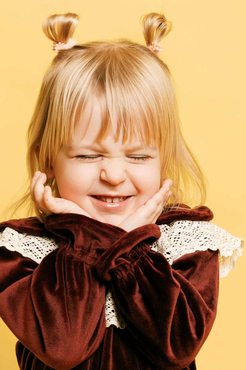 A child with two little hair buns smiling with their hands beside their face. Face of Vauva 2025.