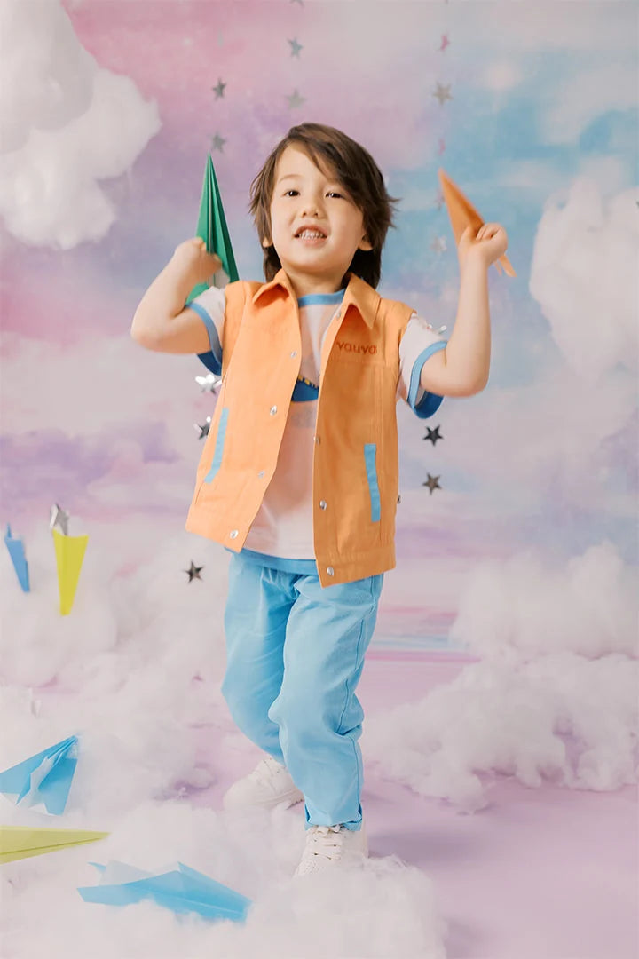 Boy wearing a white narwhal graphic tee, peach gilet and blue barrel trousers.