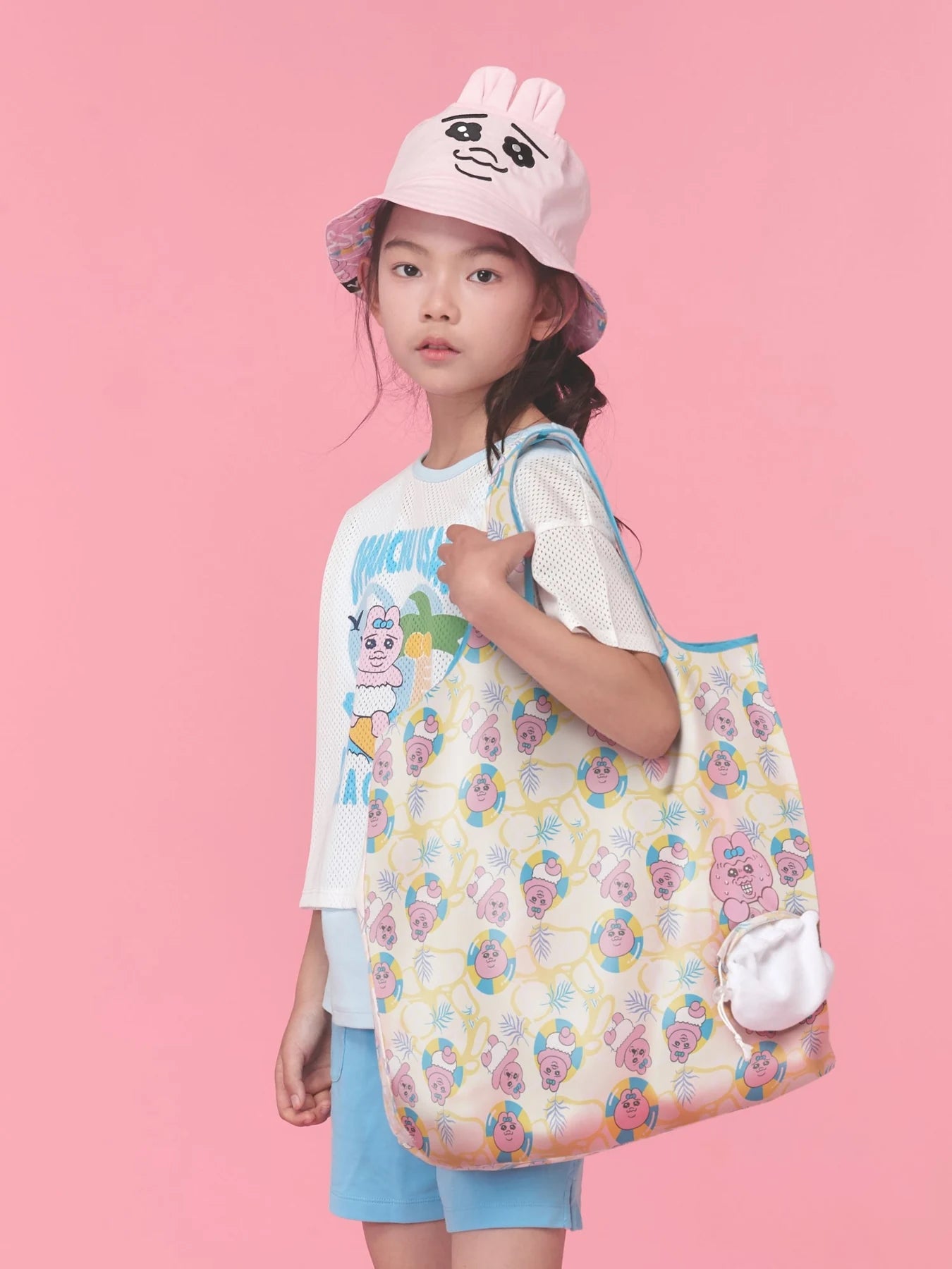 A printed drawstring tote, pink bunny hat and white tee bring the travelling companions together.