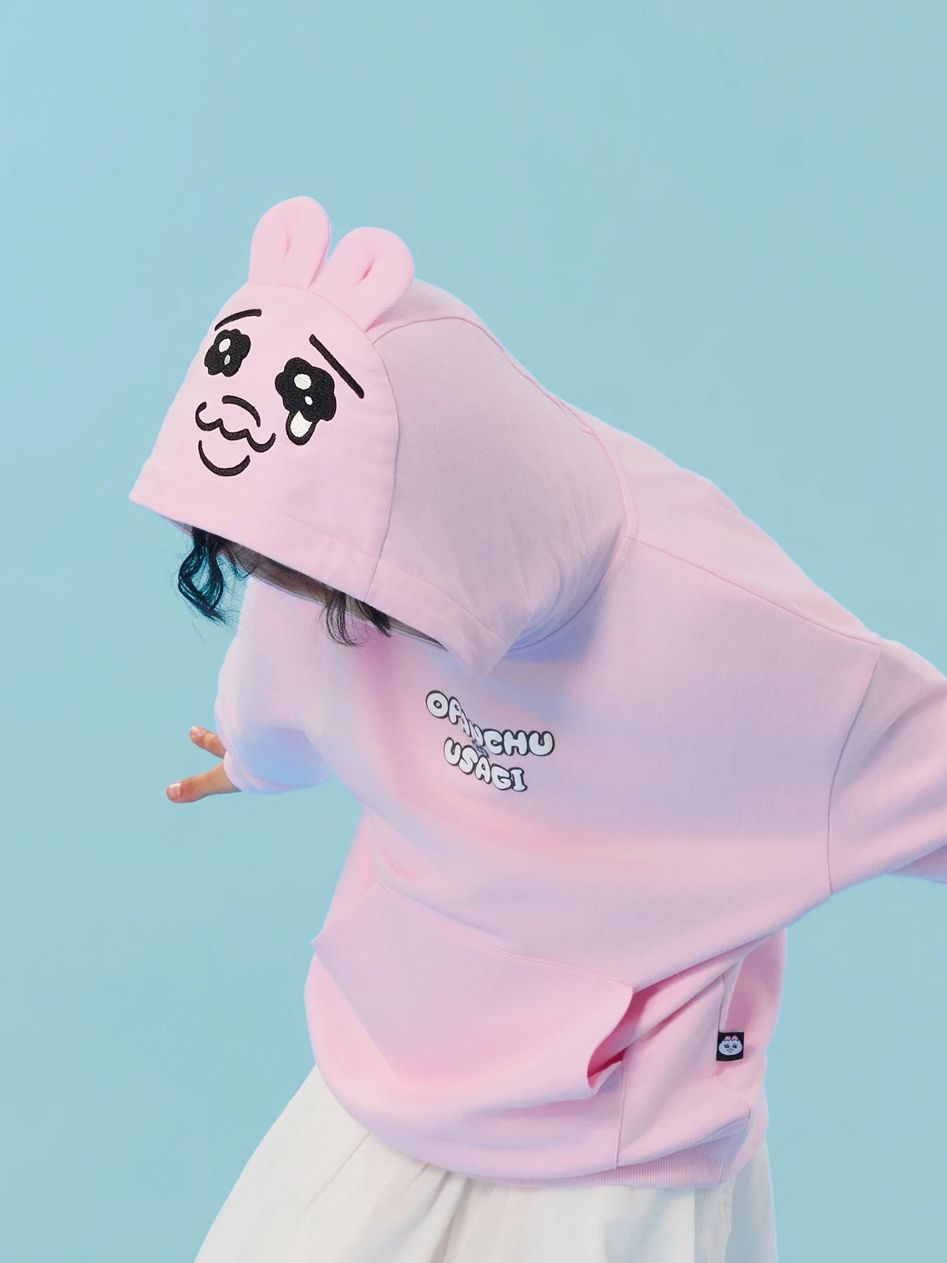 Close view of the embroidered face and bunny-ear hood on the pink sweatshirt.
