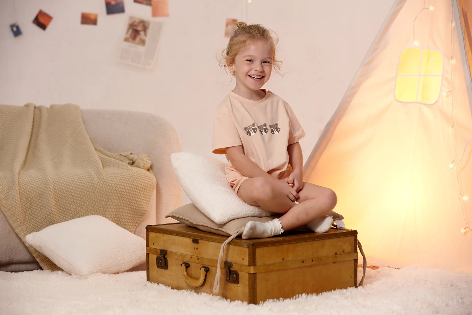 A child in the peach raccoon lounge set seated on a suitcase.
