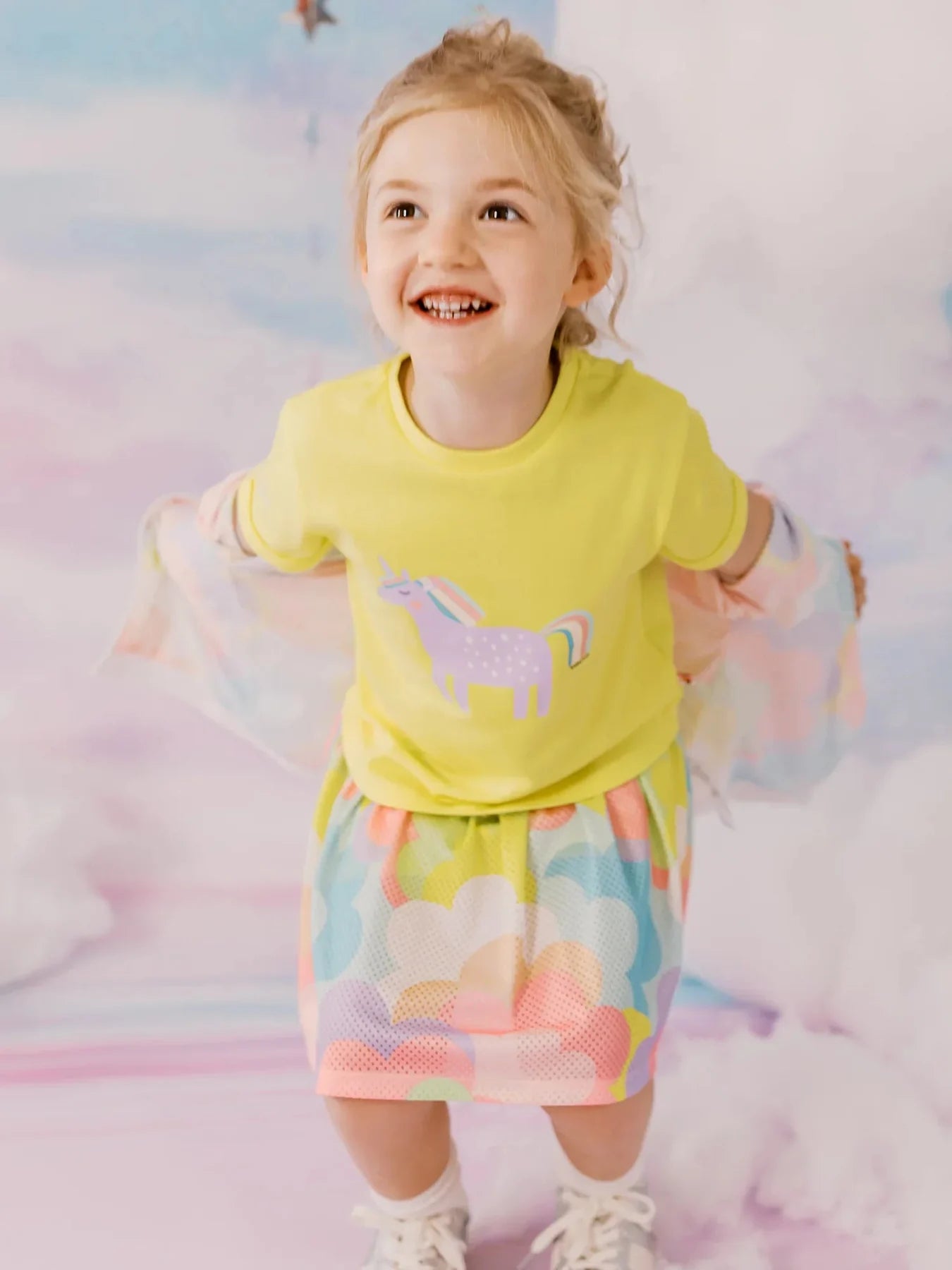 Girl wearing a yellow unicorn graphic tee and floral skirt.