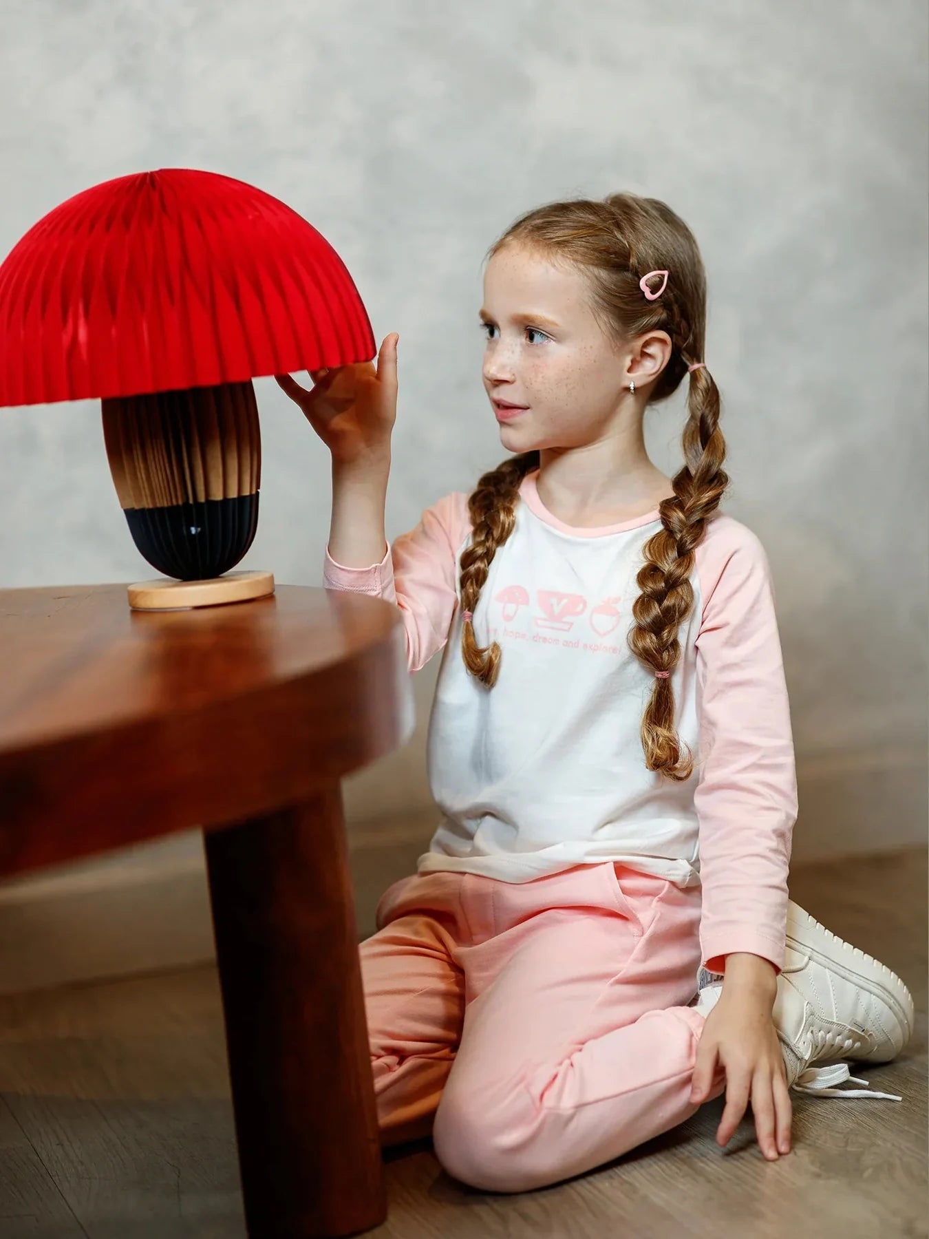 A child seated beside a mushroom prop in the pink-and-white icon raglan top.
