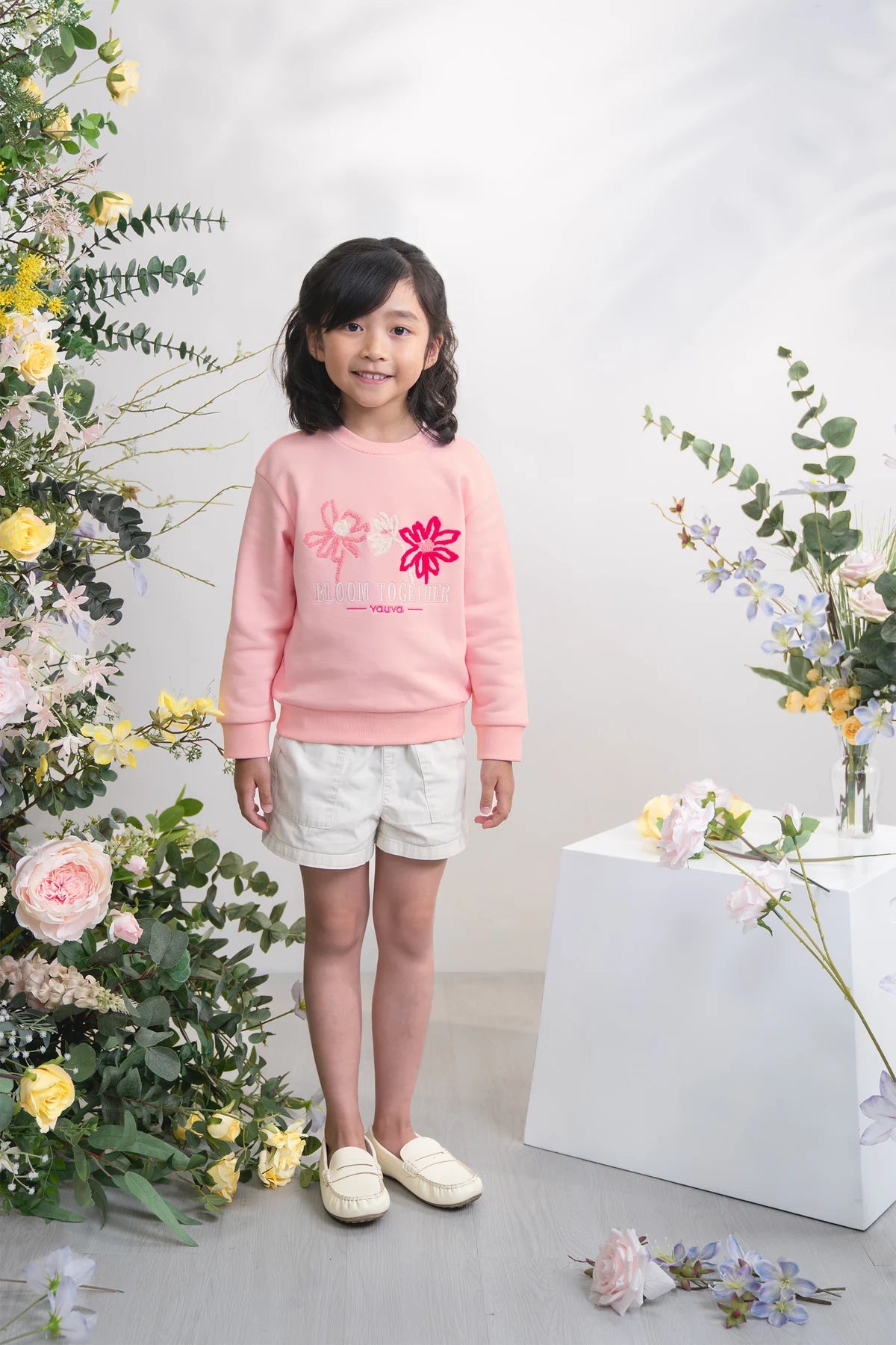 Child in a pink embroidered sweatshirt in the floral studio.