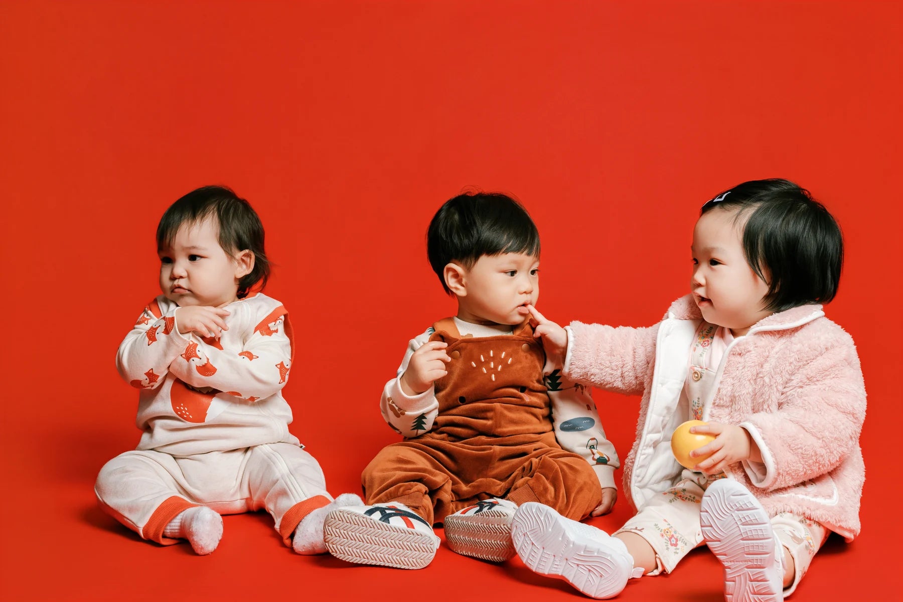 Three children sitting together on the red Face of Vauva 2025 set