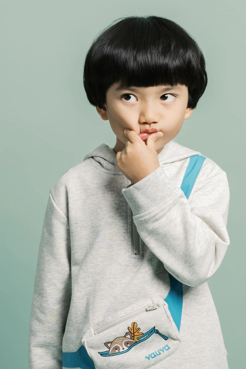 A child in a grey sweatshirt with a turquoise shoulder bag. Face of Vauva 2025.