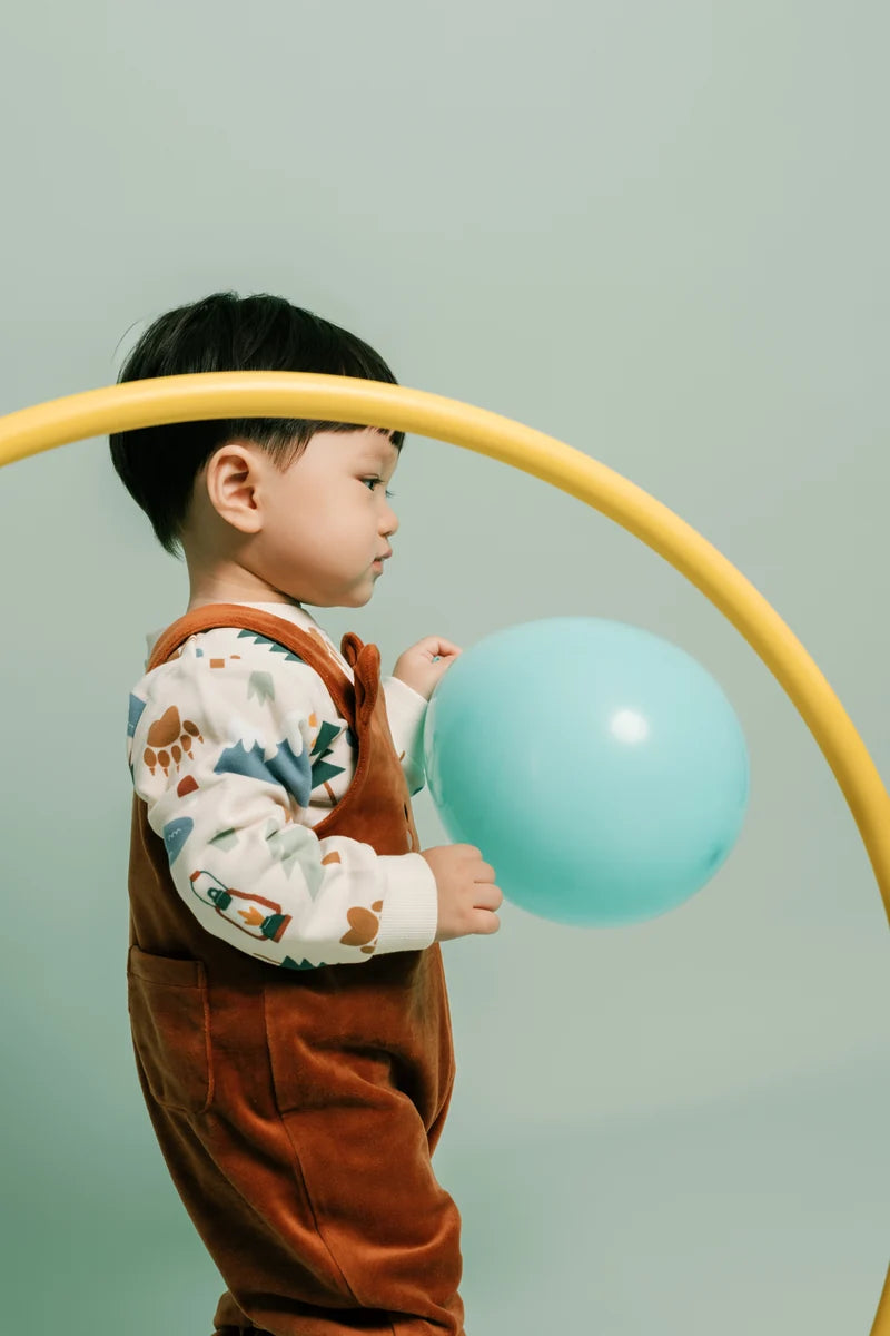 A child in rust-coloured dungarees playing with a blue balloon. Face of Vauva 2025.