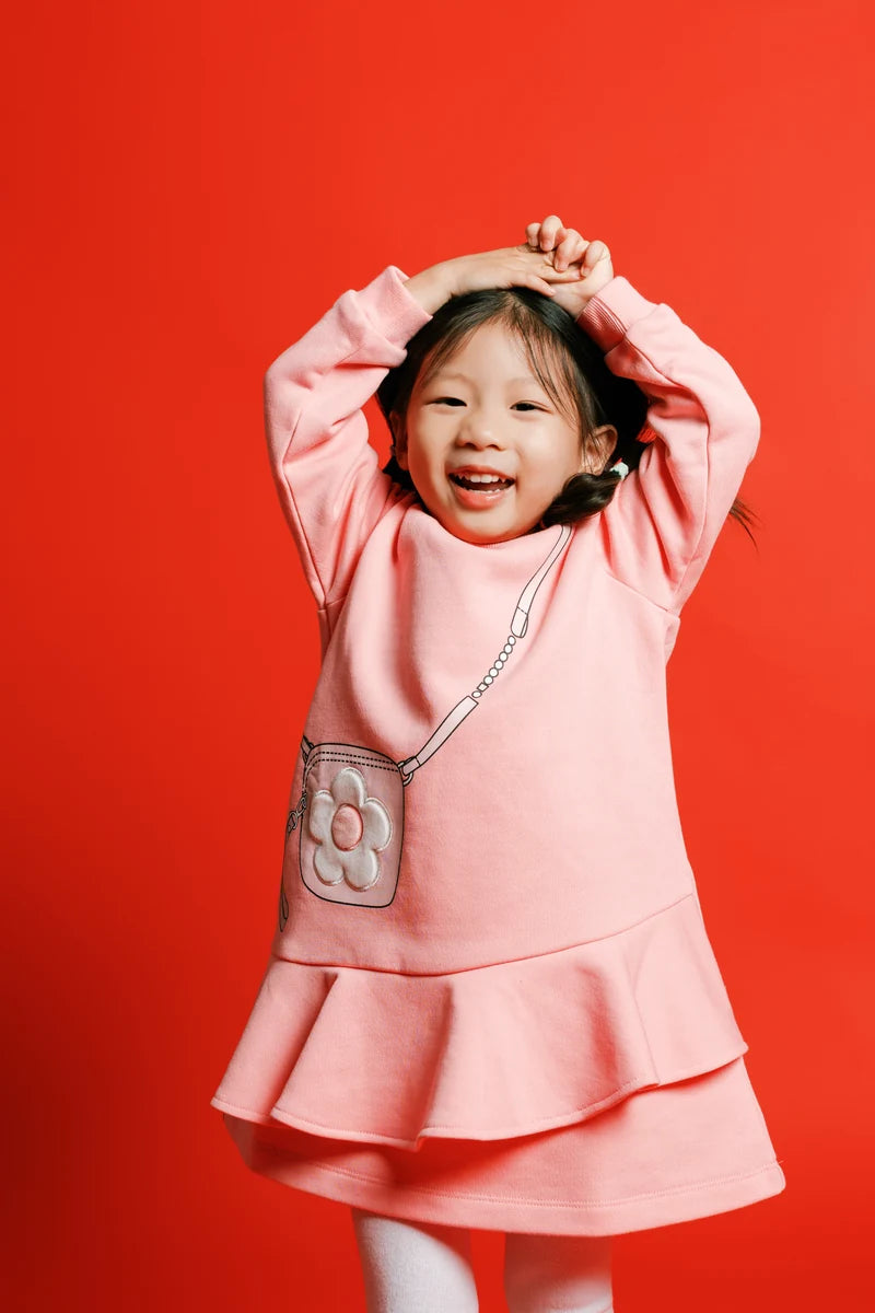 A child raising their arms above their head in a pink outfit. Face of Vauva 2025.