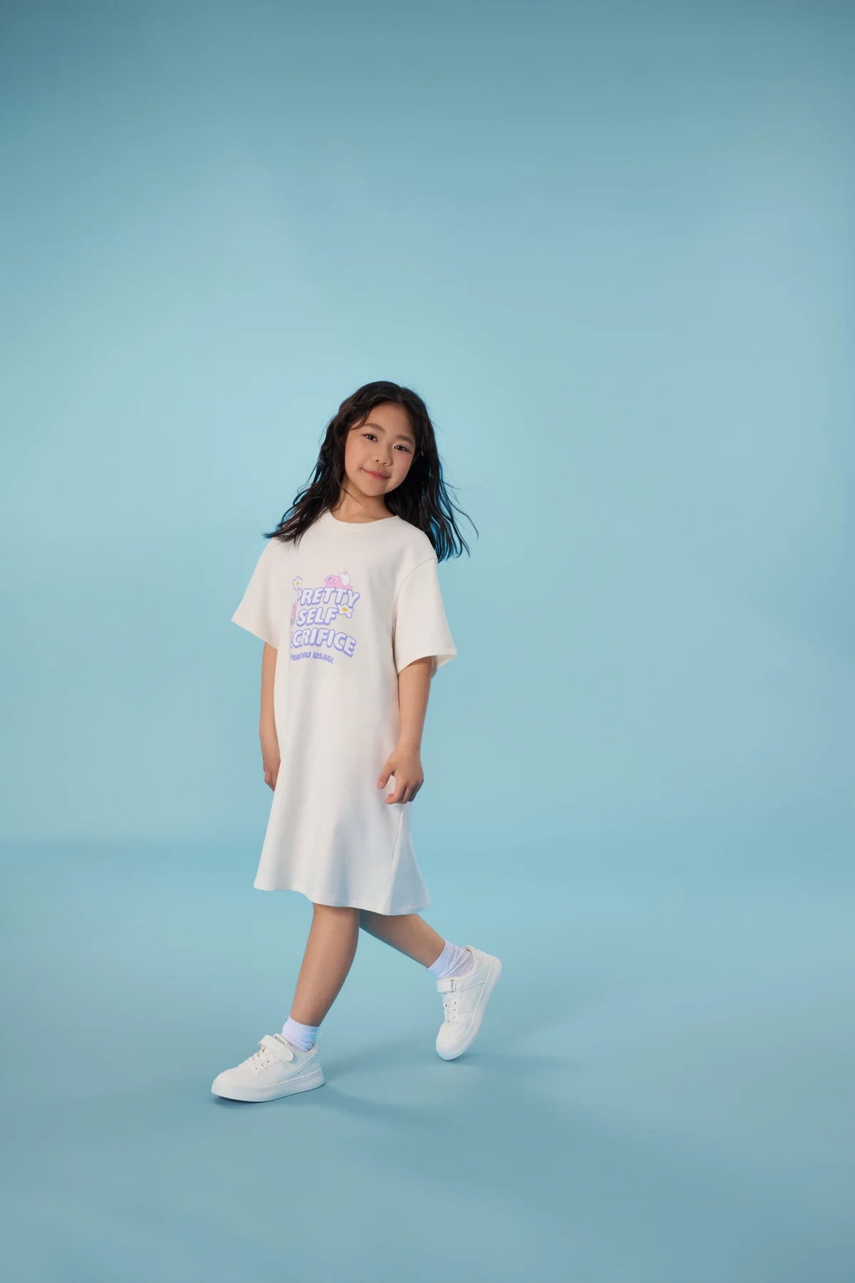 Girl wearing the white Opanchu graphic T-shirt dress against a pale blue studio background.