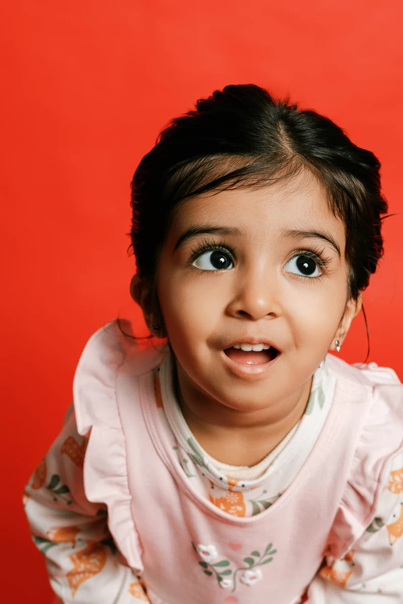 A child wearing a floral outfit and pale pink bib. Face of Vauva 2025.