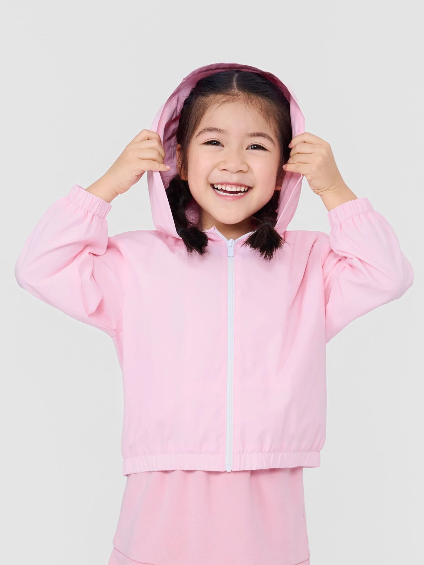 Girl holding the hood of her pink Little My lightweight jacket.
