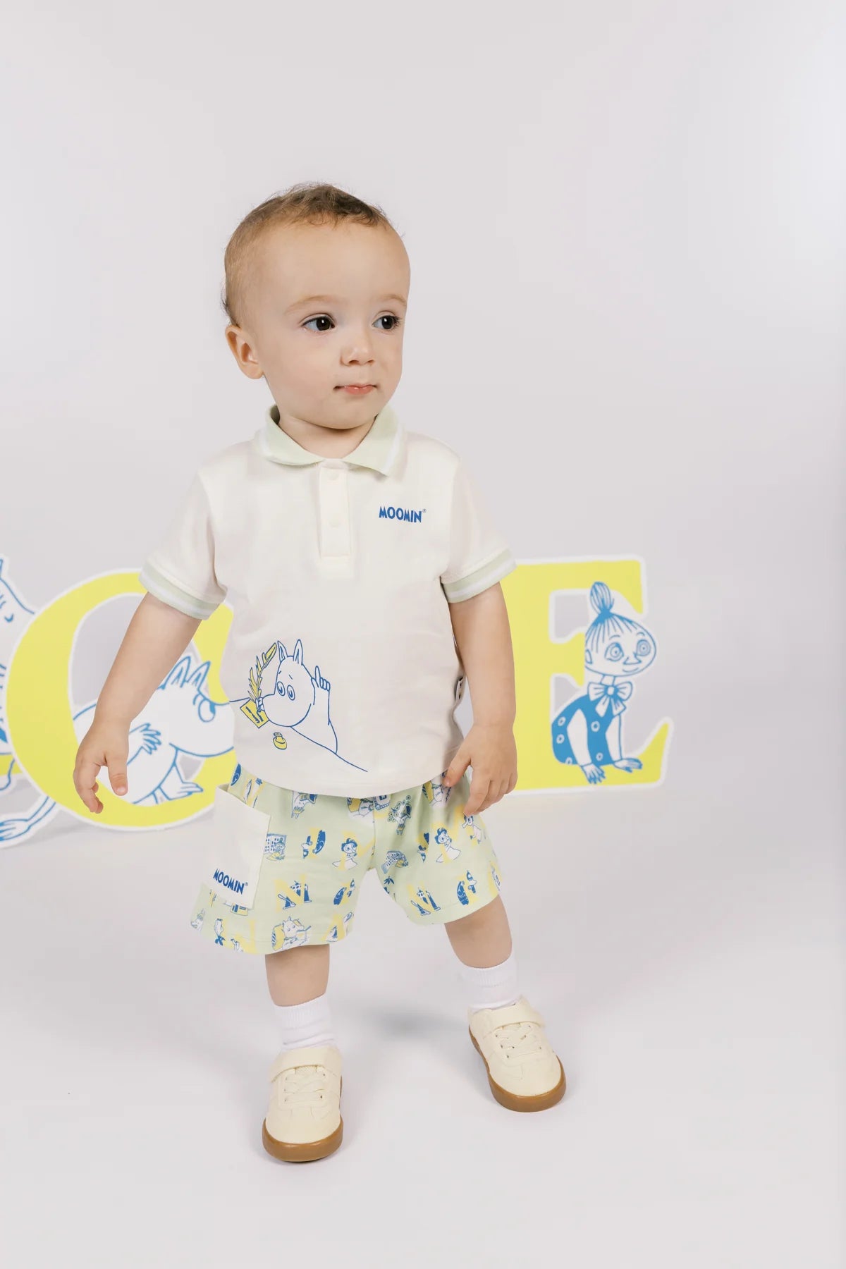 Baby wearing the ivory letter-and-character T-shirt and green printed shorts, showing the outfit from the front.