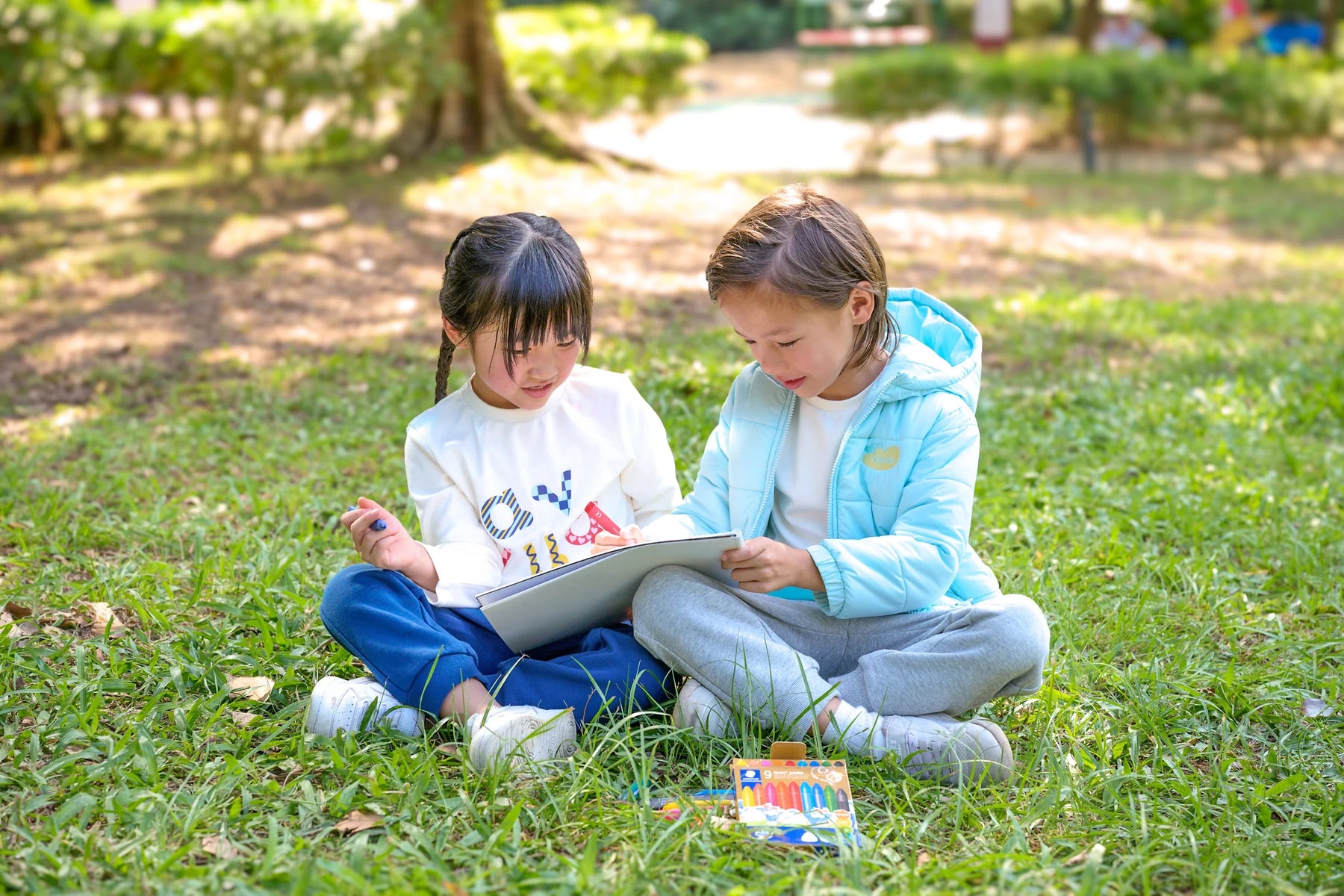 Two children drawing together on the grass, wearing Vauva FW26.