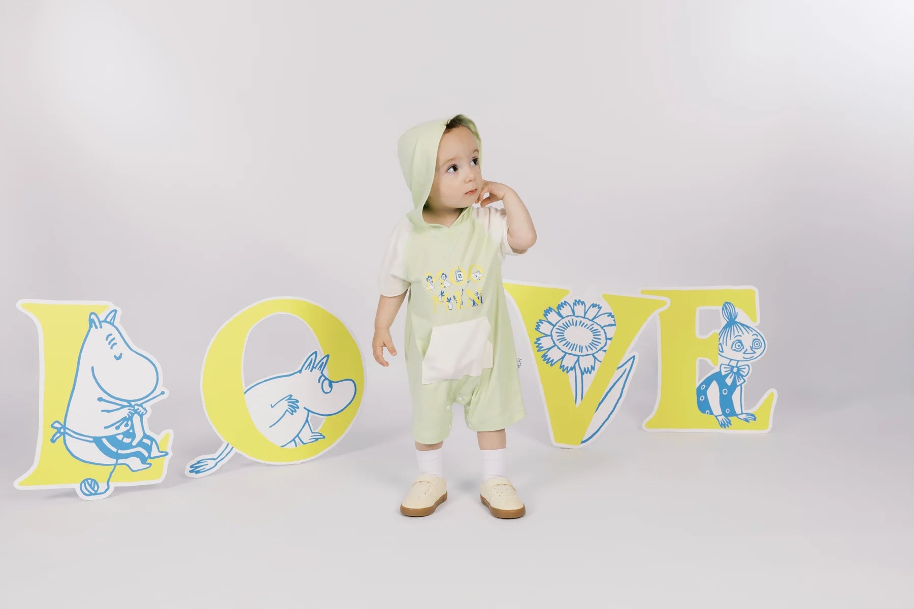 Baby in a green hooded Moomin sweatshirt romper in front of large LOVE letter props.