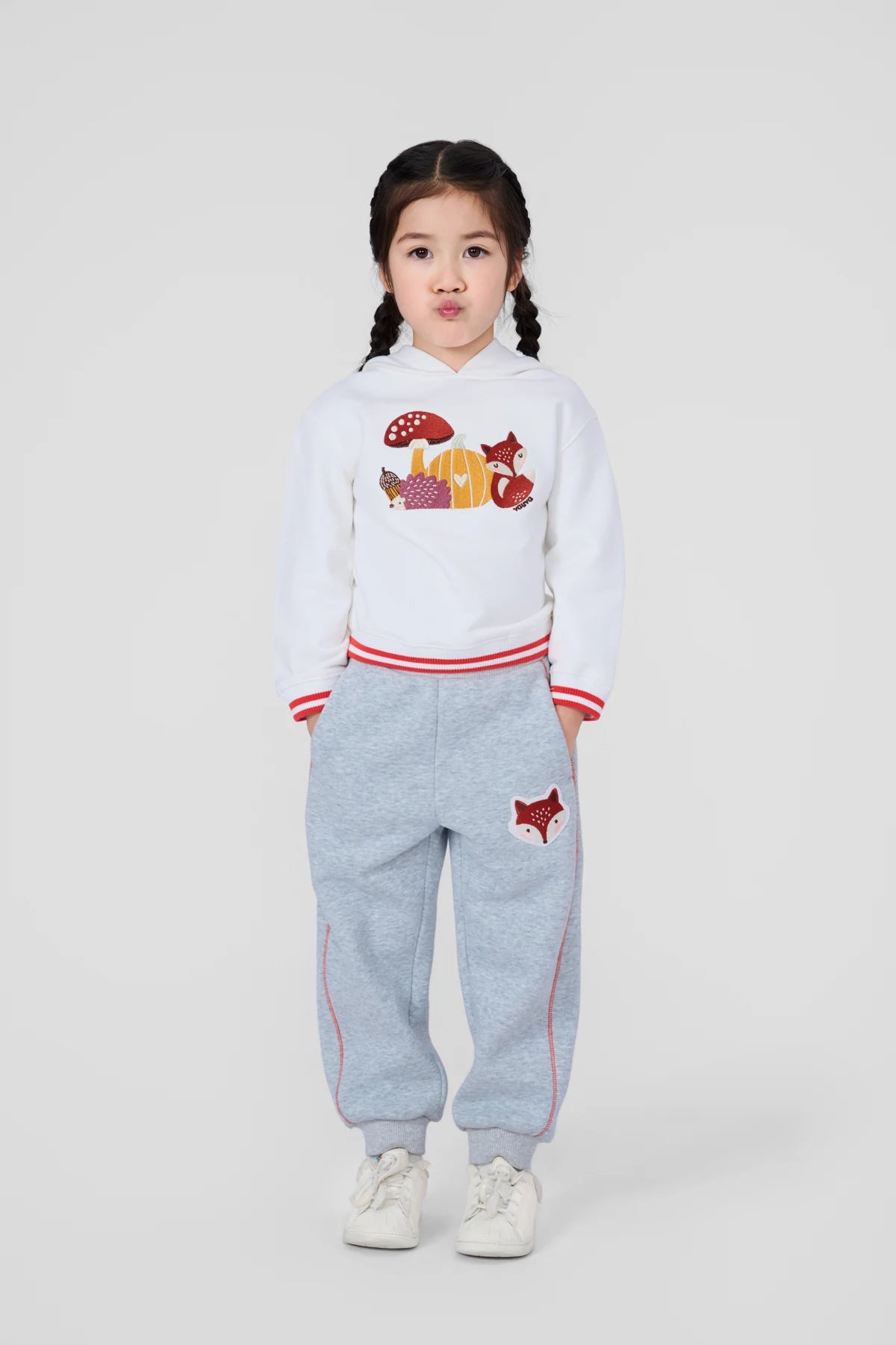 Girl wearing a white woodland embroidered hoodie and grey fox patch joggers.