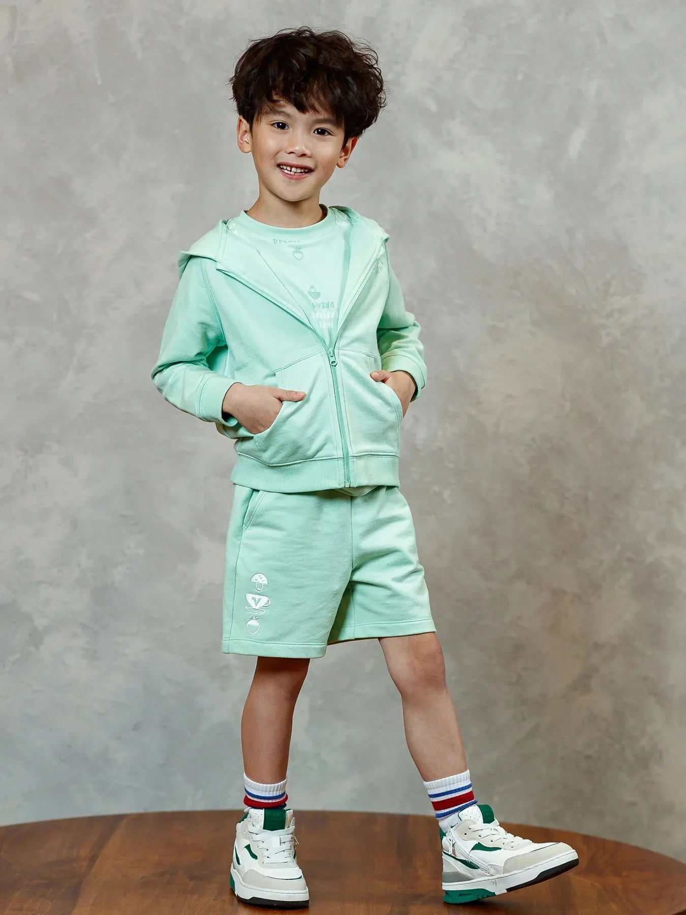 A child in the mint zip-up hoodie and matching embroidered shorts.