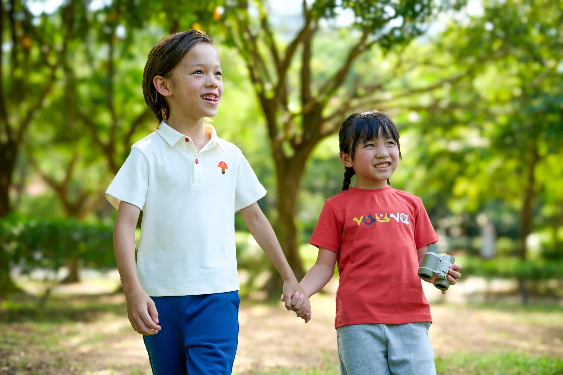 Two children walking hand in hand in the park, wearing Vauva FW26.