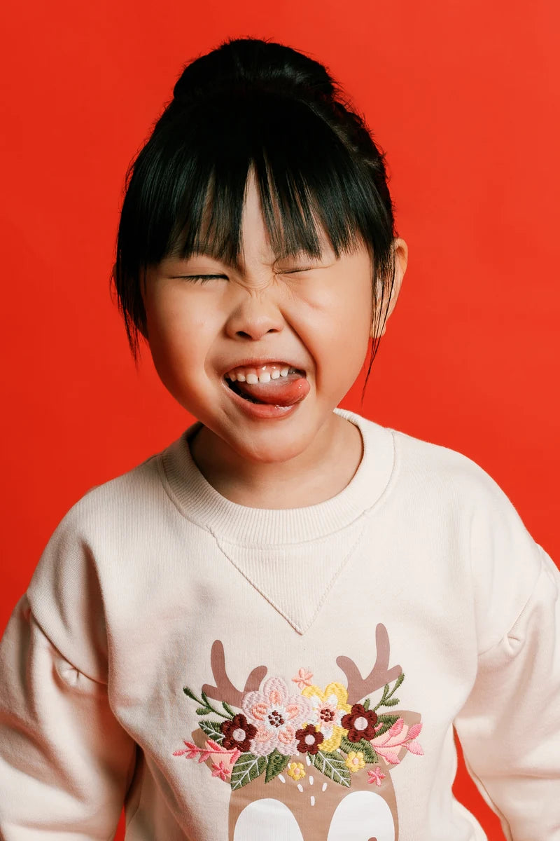 A child pulling a playful expression in a floral-print sweatshirt. Face of Vauva 2025.