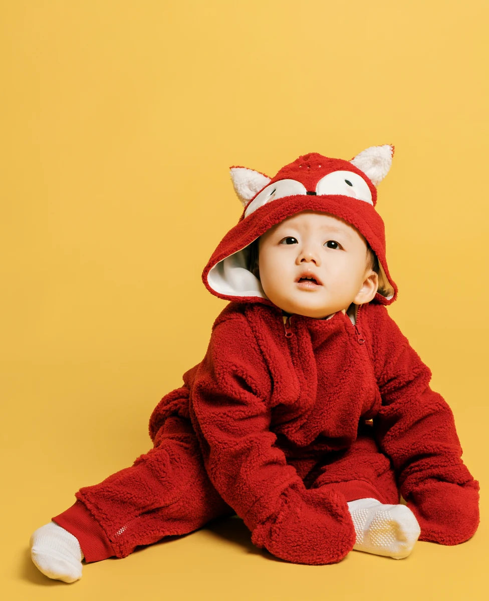 A baby in a red fox-eared hooded outfit. Face of Vauva 2025.