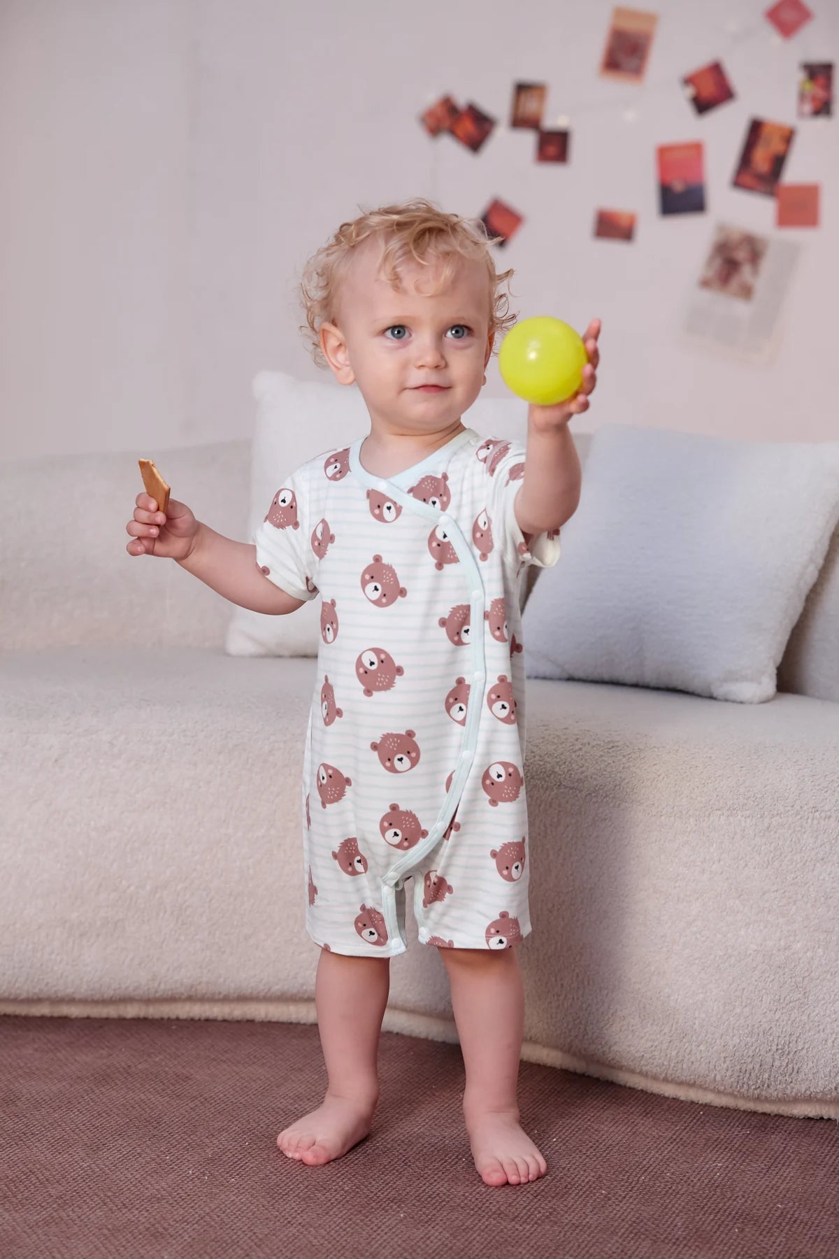 A toddler holds a toy in the bear all-over-print wrap short romper, one design in the seven-piece set.
